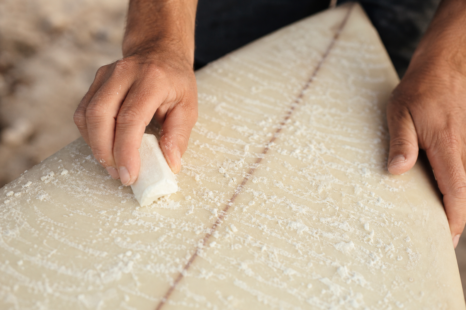 Close-up of hands applying fresh wax to a surfboard deck for better grip