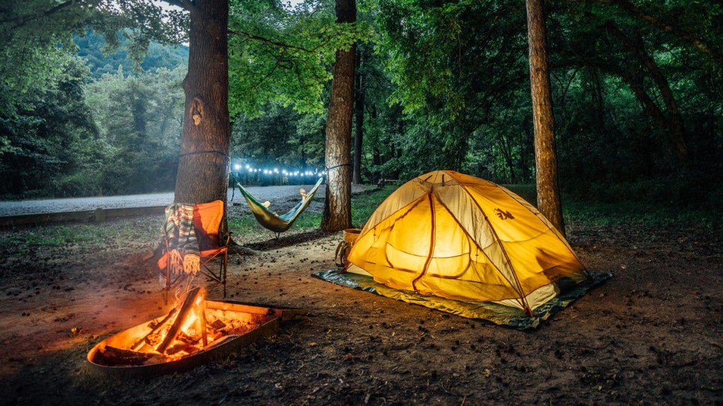 Tents and an RV at a riverside campsite with string lights glowing at dusk