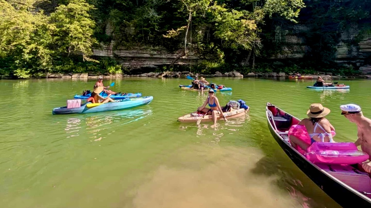 Family paddling a tandem kayak past limestone bluffs on a scenic Buffalo River float